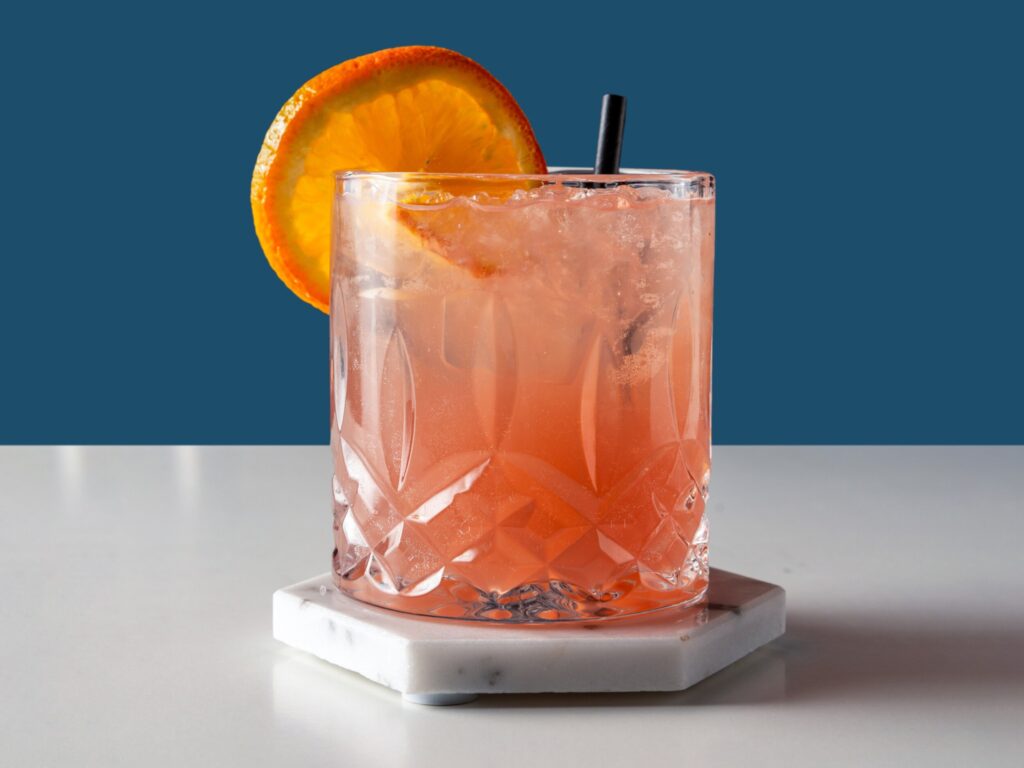 Orange cocktail i glas med is og skive appelsin.